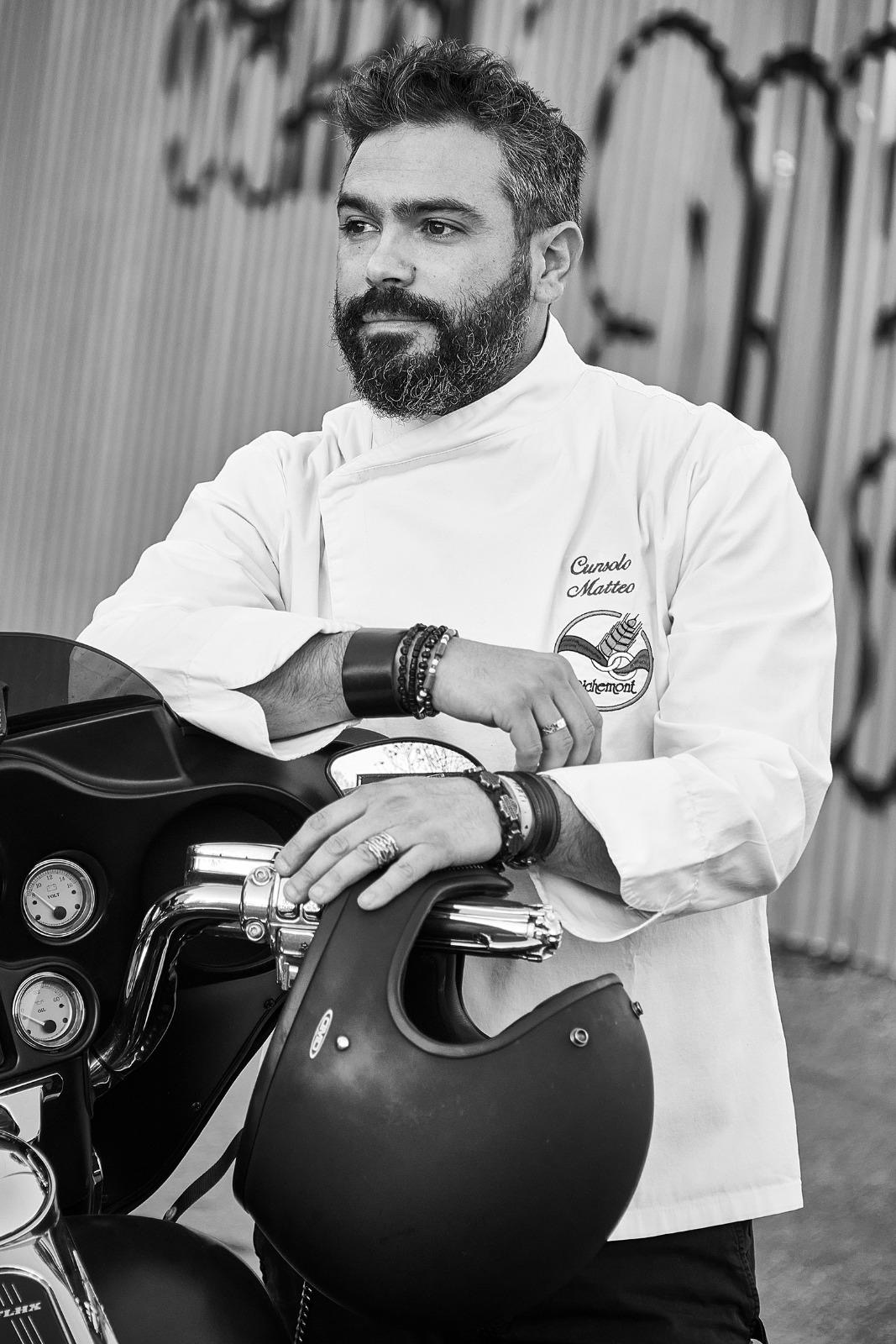 Ritratto di Matteo Cunsolo in giacca da chef appoggiato a una moto.